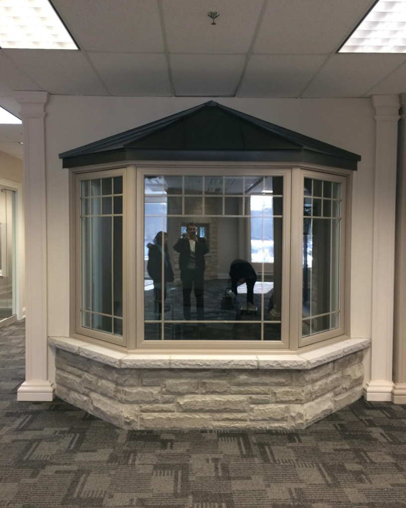 Three-panel-bay-window-in-beige-vinyl-with-grid-pattern-set-on-a-stone-base-indoor-showroom